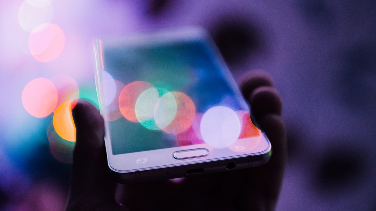A hand holding a smartphone with colourful bokeh lights visible on the screen