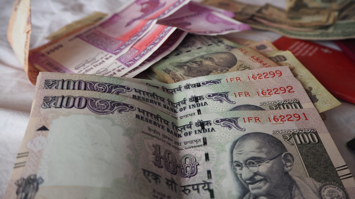 Indian 100 and 2000 rupee notes fanned out on a cloth, with US dollar notes lying behind them